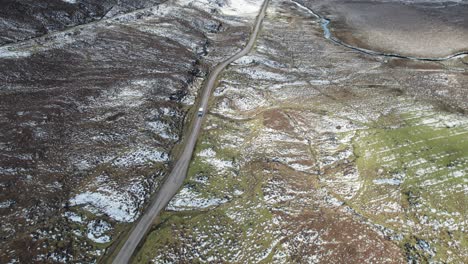 Car-driving-over-a-road-between-rural-landscape-with-snow-in-Scotland