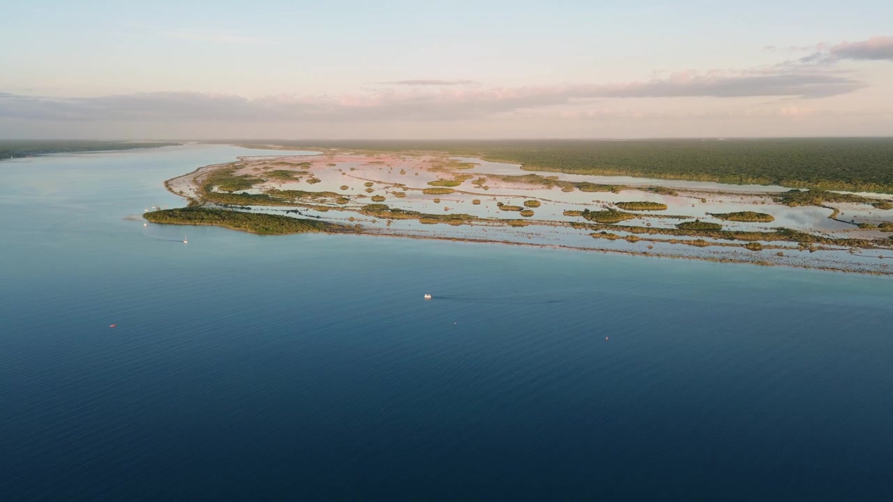 Riprese aeree con drone che panoramicano attraverso la vasta Laguna di Bacalar verso l'orizzonte, rivelando intricati schemi di zone umide di mangrovie e una barca solitaria che attraversa le calme acque azzurre in Messico.
