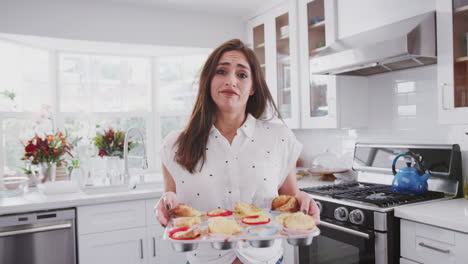 Disappointed-millennial-Hispanic-woman-presenting-cakes-to-camera-after-a-baking-disaster,-close-up