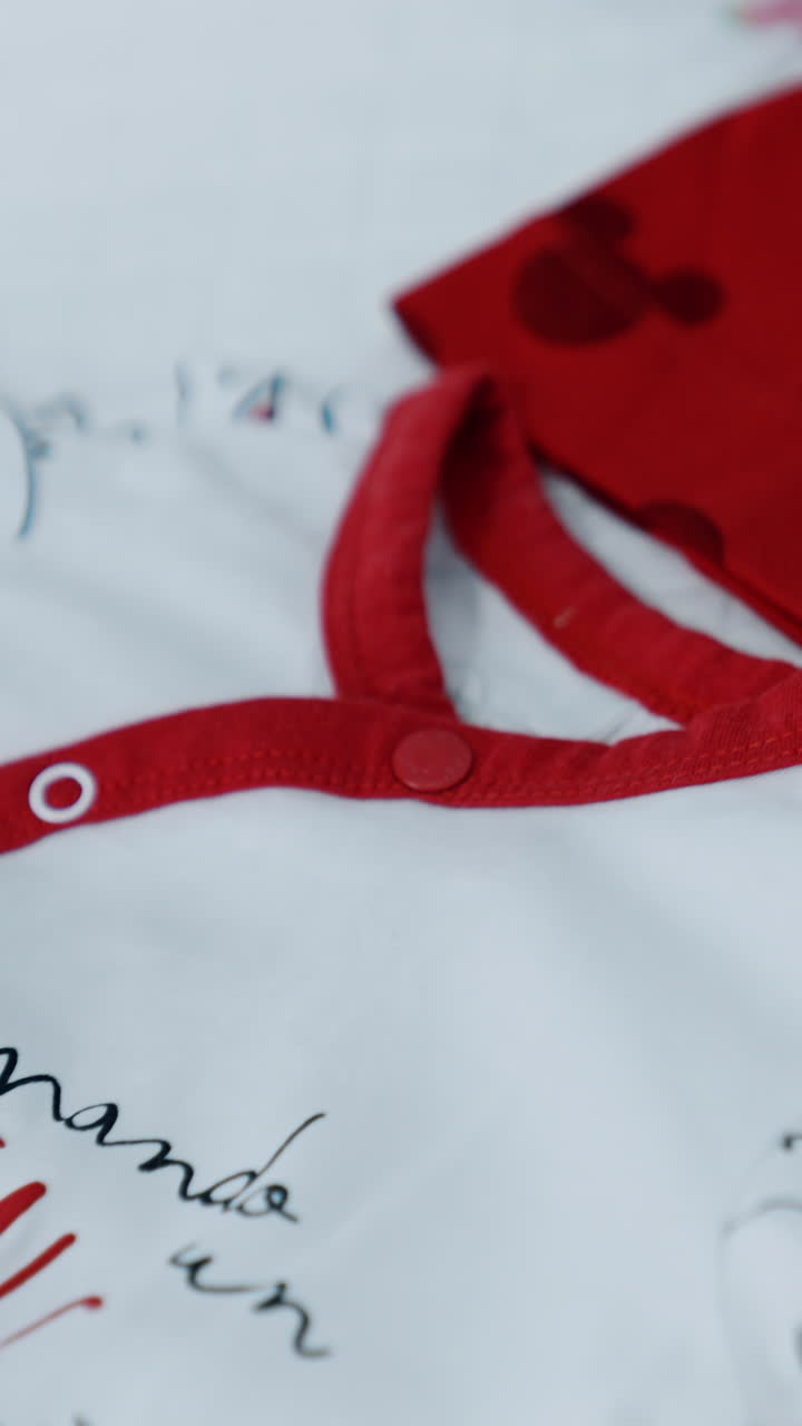 Red cap and white bodysuit with letters on the table. Pieces of clothes for a newborn child. Close up. Vertical video