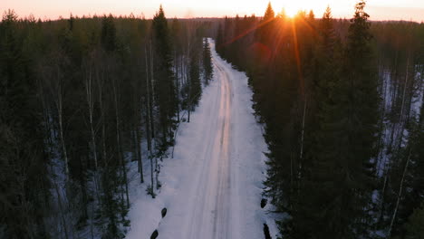 Drone-shot-of-slippery-ice-covered-narrow-road-in-the-middle-of-a-forest-by-sunset