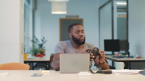 African-man-connecting-camera-to-notebook.-Man-recording-photos-to-computer