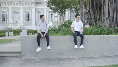 Two asian friends chatting while sitting on a ledge in front of the National Museum of Singapore on a hot summer bright day