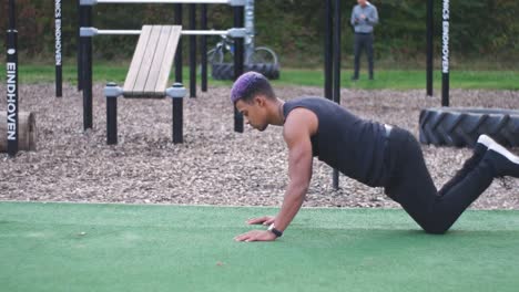 dolly shot going around a muscular guy who does knee push ups in an outdoor callisthenics sports park