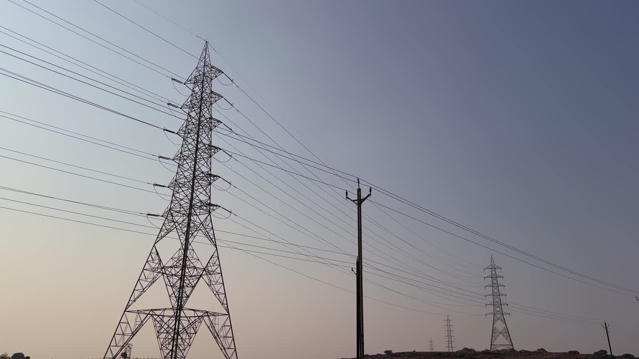 Static shot of tall transmission towers and power lines stretching across the sky, silhouetted against a soft early-morning gradient with calm atmosphere