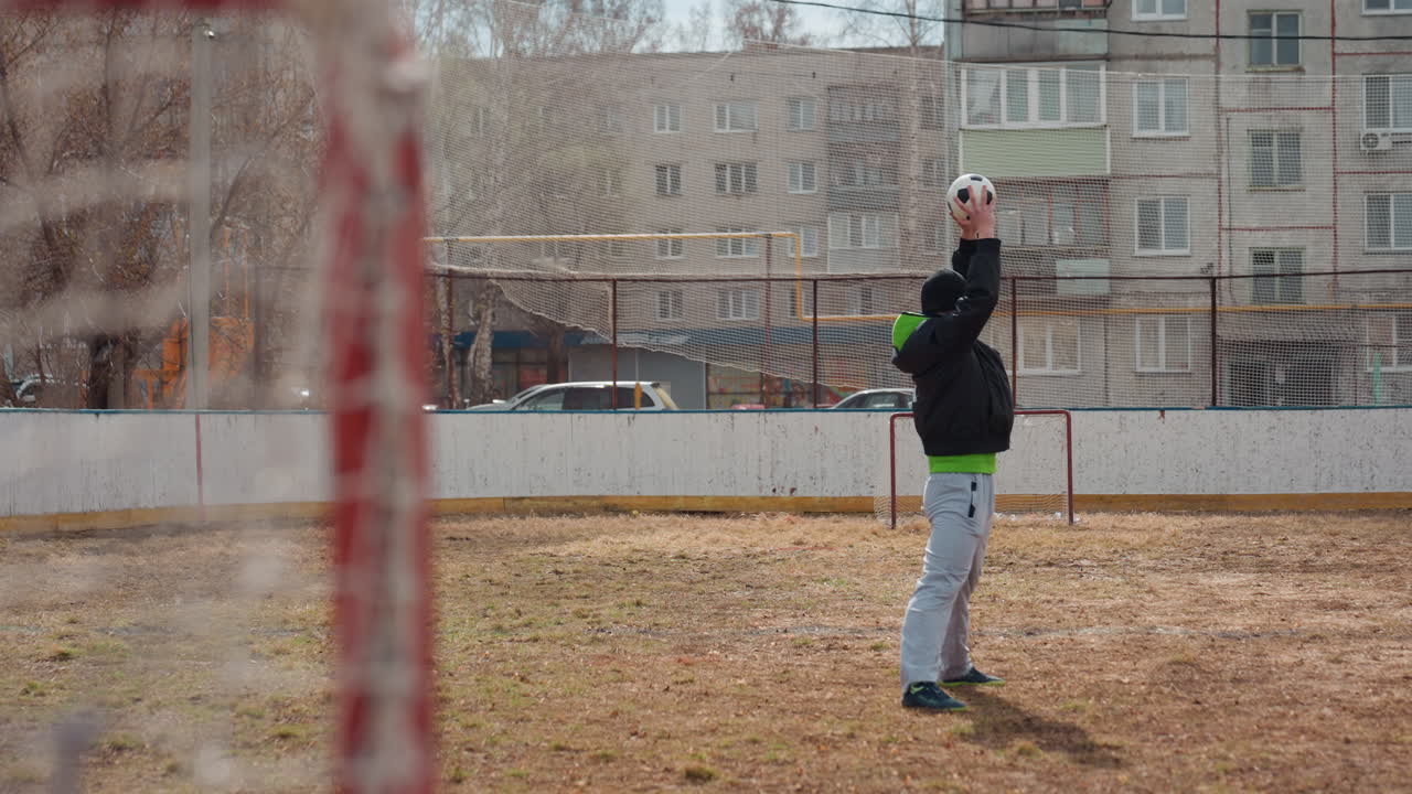 practicing handson catching routine outdoors, repetitive training session for goalkeeper on city field, goalkeeper honing reflexes by catching balls repeatedly on deserted urban sports ground