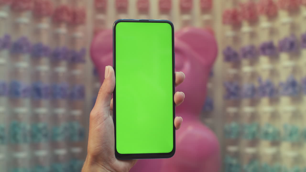 Hand holding a smartphone with a green screen in a colorful, blurred background