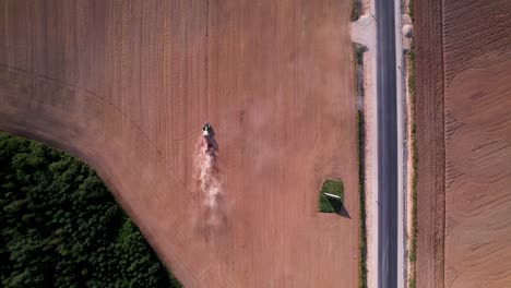 Sideview-of-tractor-ploughing-across-dry-field-next-to-highway-in-midday