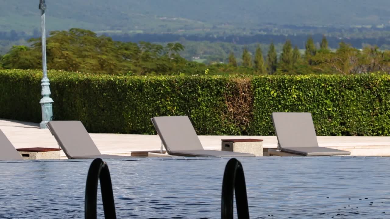 Relax by the pool with lounge chairs and lush greenery under a clear sky.