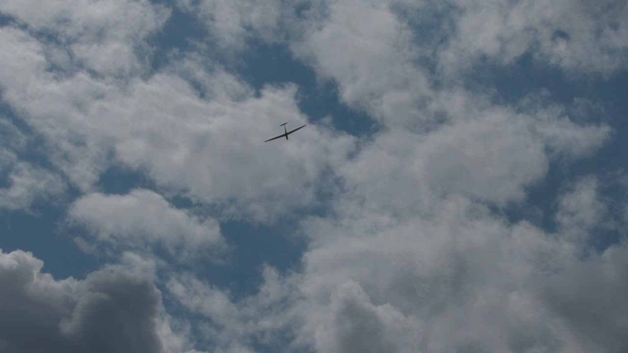 small white airplane flies on bright blue sky with clouds