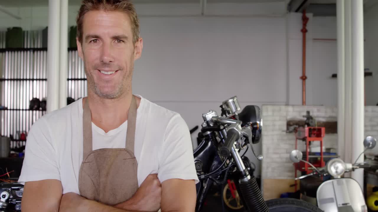 Male mechanic standing with arms crossed in motorbike repair garage 4k