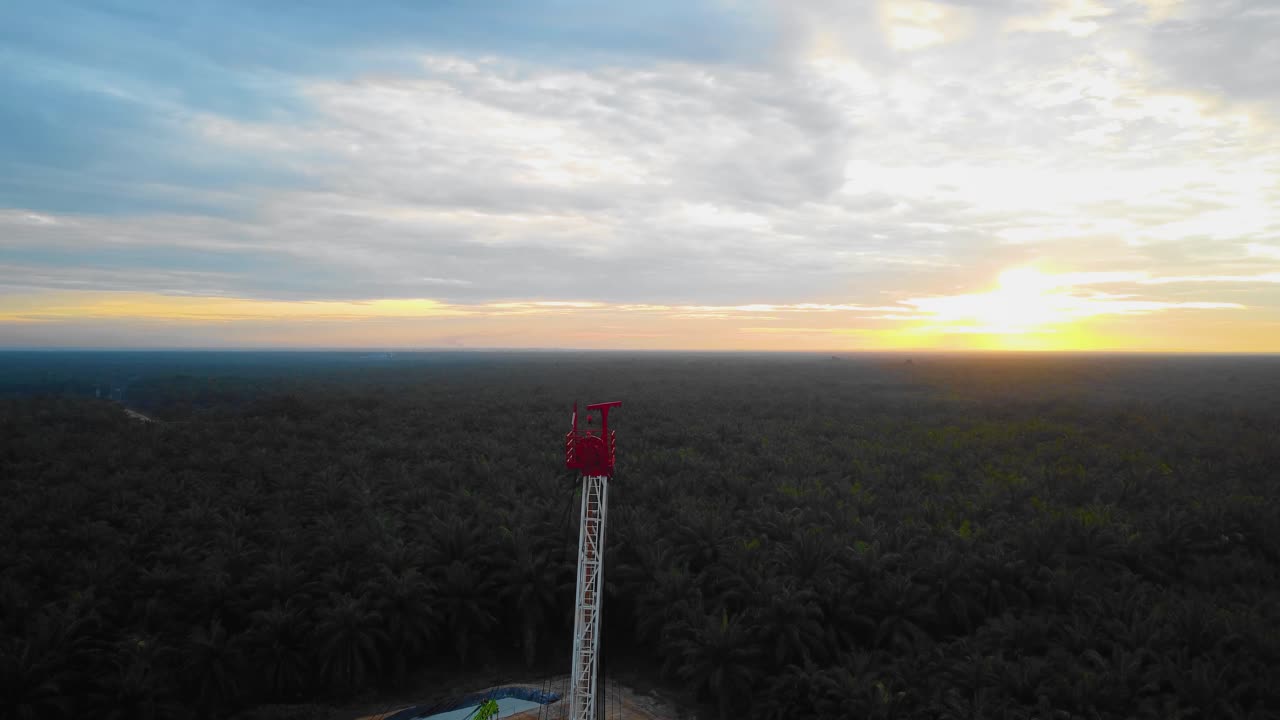 imágenes cinematográficas de drones de la estructura del equipo de la plataforma de perforación en tierra para la exploración y explotación de petróleo en medio de la jungla rodeada de palmeras durante la puesta de sol y el alto precio del petróleo