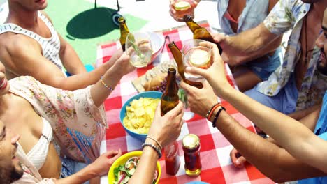 Group-of-happy-friends-toasting-beer-bottles-and-glasses-at-outdoors-barbecue-party