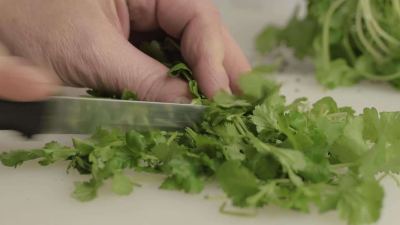 Hands cutting fresh coriander herb in kitchen with knife close up shot