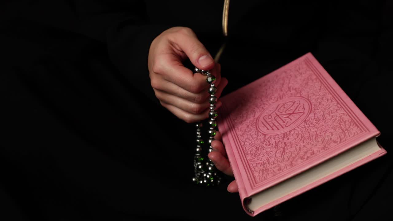 Filmato di una donna musulmana che tiene in mano un Corano rosa e prega con il suo tasbeeh, il rosario islamico
