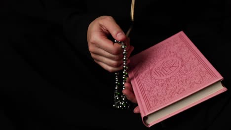 footage of a muslim woman holding a pink quran and praying on her tasbeeh, the prayer beads