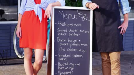 Waiter-and-woman-standing-with-menu-board-outside-the-cafÃ©