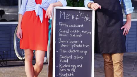 waiter and woman standing with menu board outside the cafã©