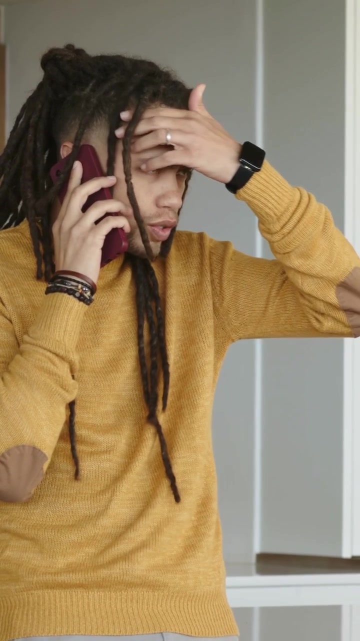 Vertikal video: Telefonen ringer, mann i sennepsgul strikkegenser tenker, gnir seg i pannen, roer seg på kjøkkenet.