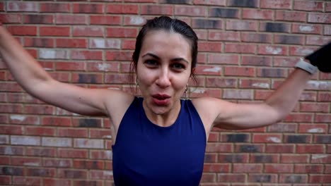 mujer en buena forma física haciendo un ejercicio con mancuernas de pie contra la pared de ladrillo rojo