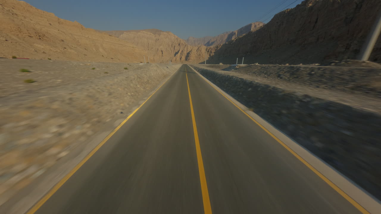 FPV drone flies low above a desert road in Hatta, with its shadow visible on the asphalt. As the shot ends, the drone begins to ascend smoothly