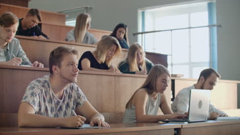 En-El-Aula,-Estudiantes-Multiétnicos-Escuchando-A-Un-Profesor-Y-Escribiendo-En-Cuadernos.-Los-Jóvenes-Inteligentes-Estudian-En-La-Universidad.