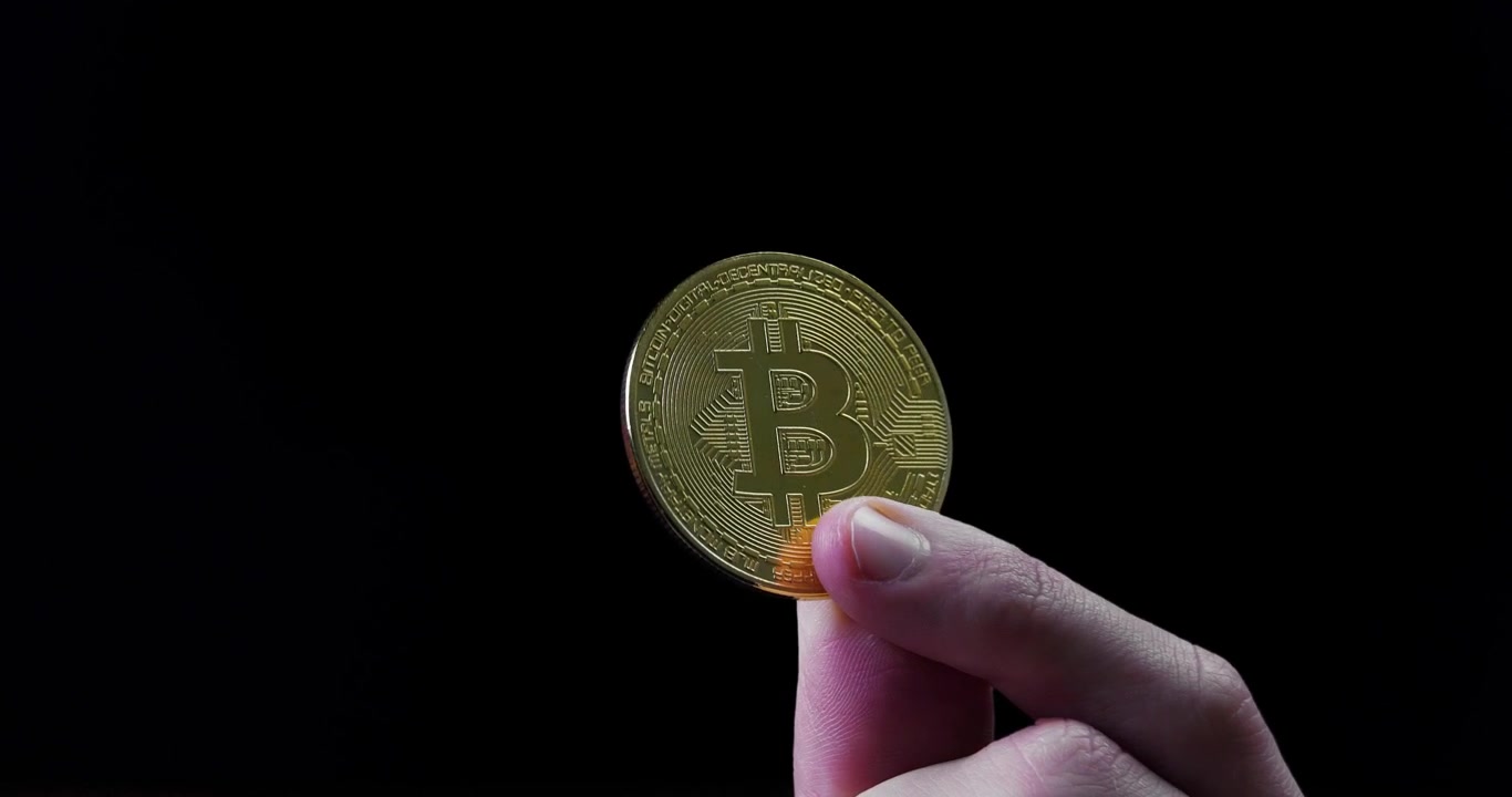Mano che tiene un Bitcoin dorato e brillante con sfondo nero