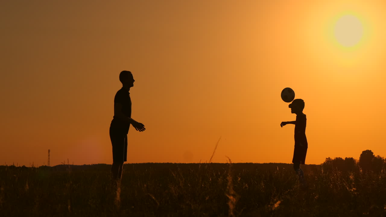 Father and son playing football in the park at sunset silhouettes against the backdrop of a bright sun slow-motion shooting.