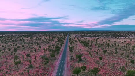 a straight road cutting through the red outback desert heading towards the horizon