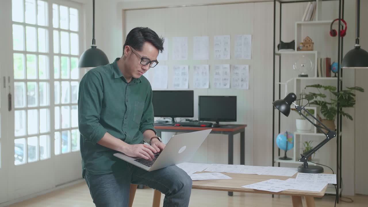 Creative Designer Sits On His Desk Holds Laptop On The Knees And Working On The Project . Creative Designe And Gaming Content Development Studio