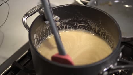 a young girl stirs a caramel mix heating up on the stove while baking millionaire shortbread cookies-3