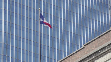 a texan flag blowing in the wind in front of a tall glass office building in downtown houston, texas