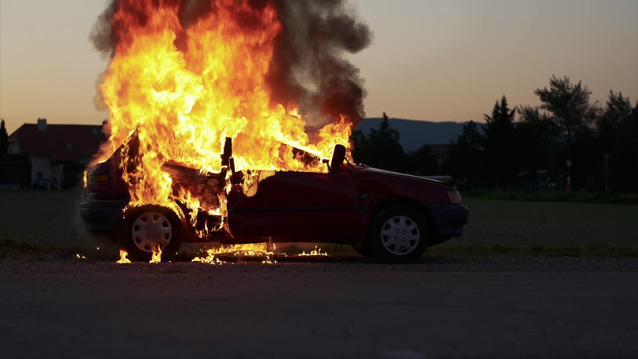 Burning car in the evening hours, long shot, from the side - Slow Motion