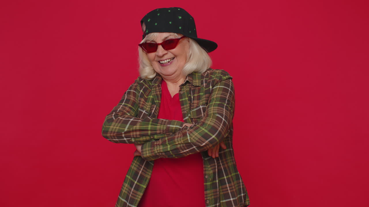 선글라스를 입은 셔츠를 입은 매혹적인 즐거운 세련된 고령 여성, 분홍색 벽에 매력적인 미소