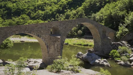 panorámica de la izquierda a la derecha del puente del diablo y el río arda, situado al pie de las montañas rodope en ardino, bulgaria