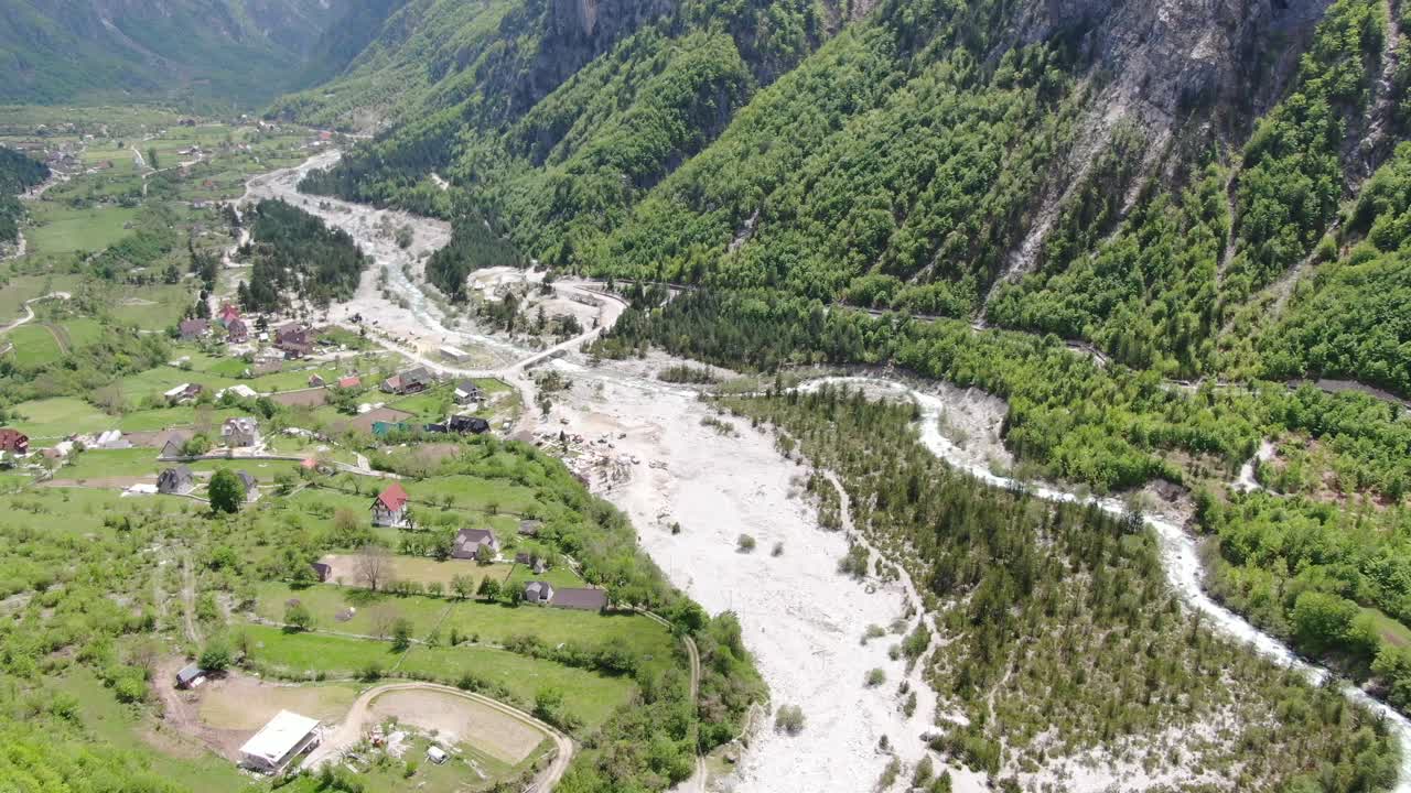 vista de aviones no tripulados en albania en los alpes volando sobre un valle verde con pequeñas casas y un río que cruza en el
