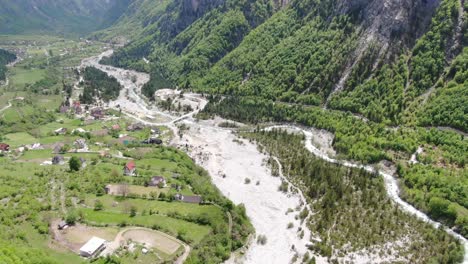 Drone-view-in-Albania-in-the-alps-flying-over-a-green-valley-with-small-houses-and-a-river-crossing-by-in-Theth