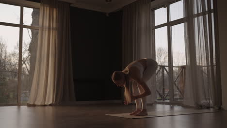 Lens-flare-:A-young-woman-in-white-sportswear-is-stretching-with-a-large-hall-with-large-windows-in-a-slow-motion-scheme-the-sun's-rays-shine-through-the-window.-Healthy-lifestyle-healthy-morning