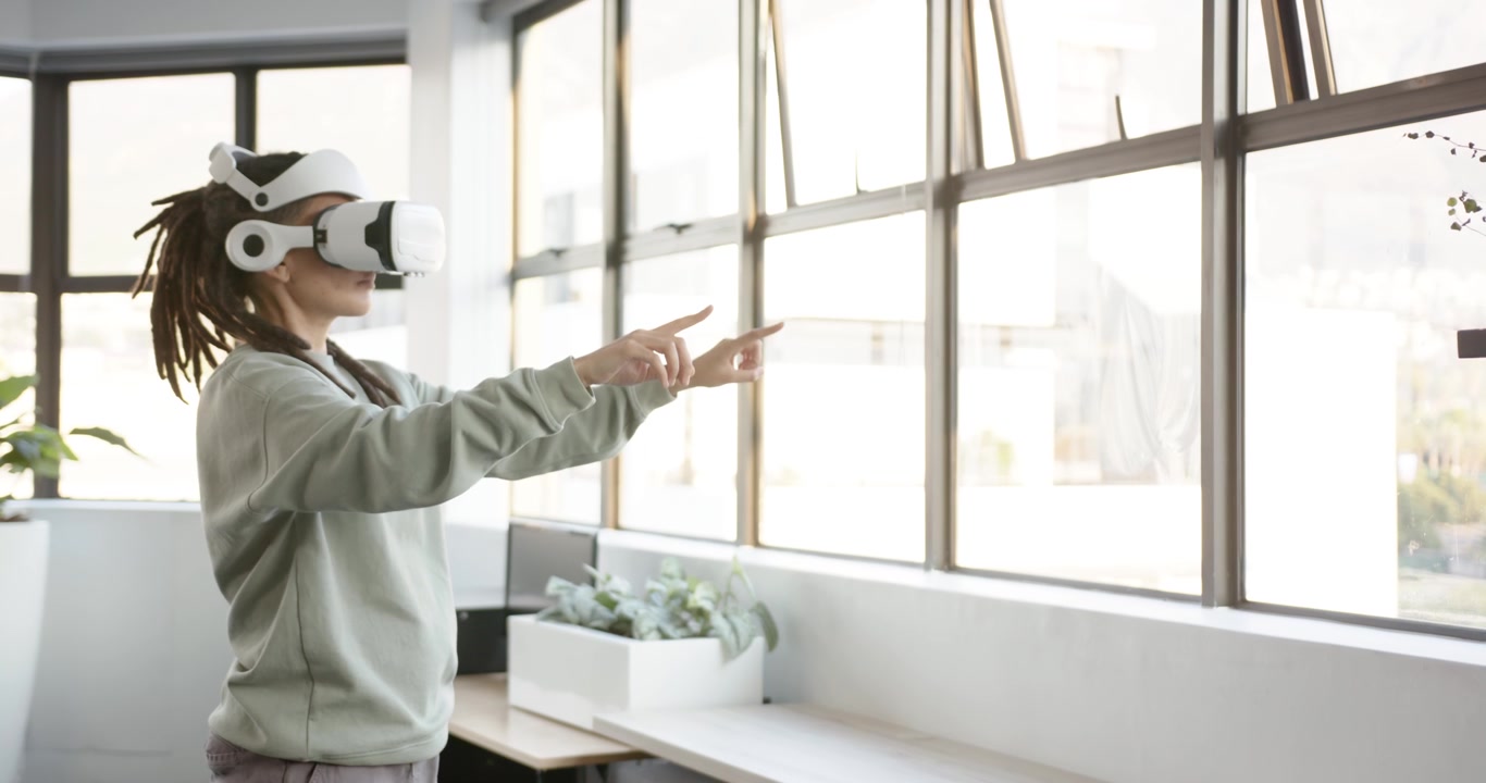 Adulto africano non binario con visore VR che si attiva, gesticolando per selezionare tramite finestre a griglia.