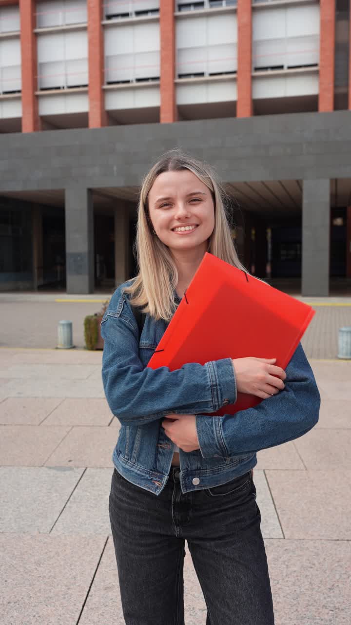 Giovane studentessa sorridente che tiene delle cartelle nel campus.