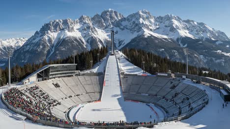spectacular winter sports arena surrounded by majestic snow-capped mountains, set against a clear blue sky, ideal for thrilling ski competitions and events