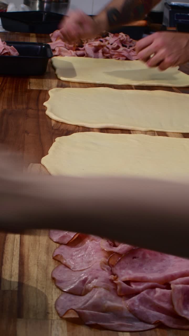 Primo piano verticale di una mano che prepara pan de jamon con prosciutto su un tavolo di legno