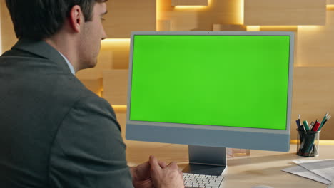 businessman looking at a green screen computer monitor in an office