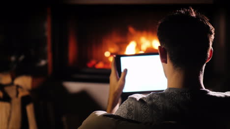 A-Man-Is-Relaxing-By-The-Fireplace-At-Home-Using-A-Tablet