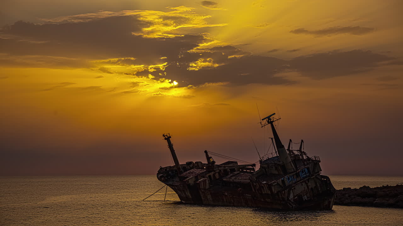 un lapso de tiempo de la puesta de sol dorada con un barco naufragado en primer plano cerca de pegeia, chipre