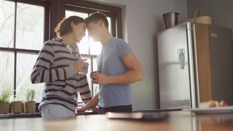 happy diverse male couple drinking coffee and embracing in kitchen