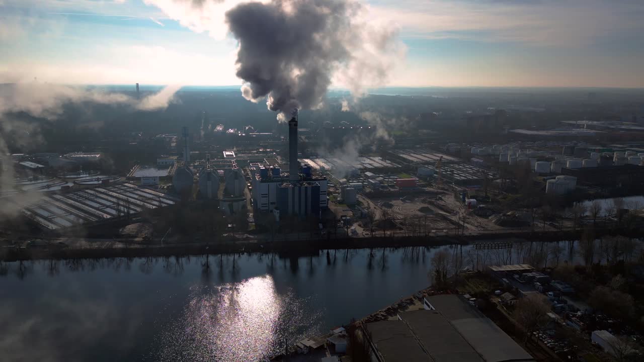 Industrial chimneys emitting white smoke over city skyline under blue sky, concept of pollution. Amazing aerial view flight descending drone