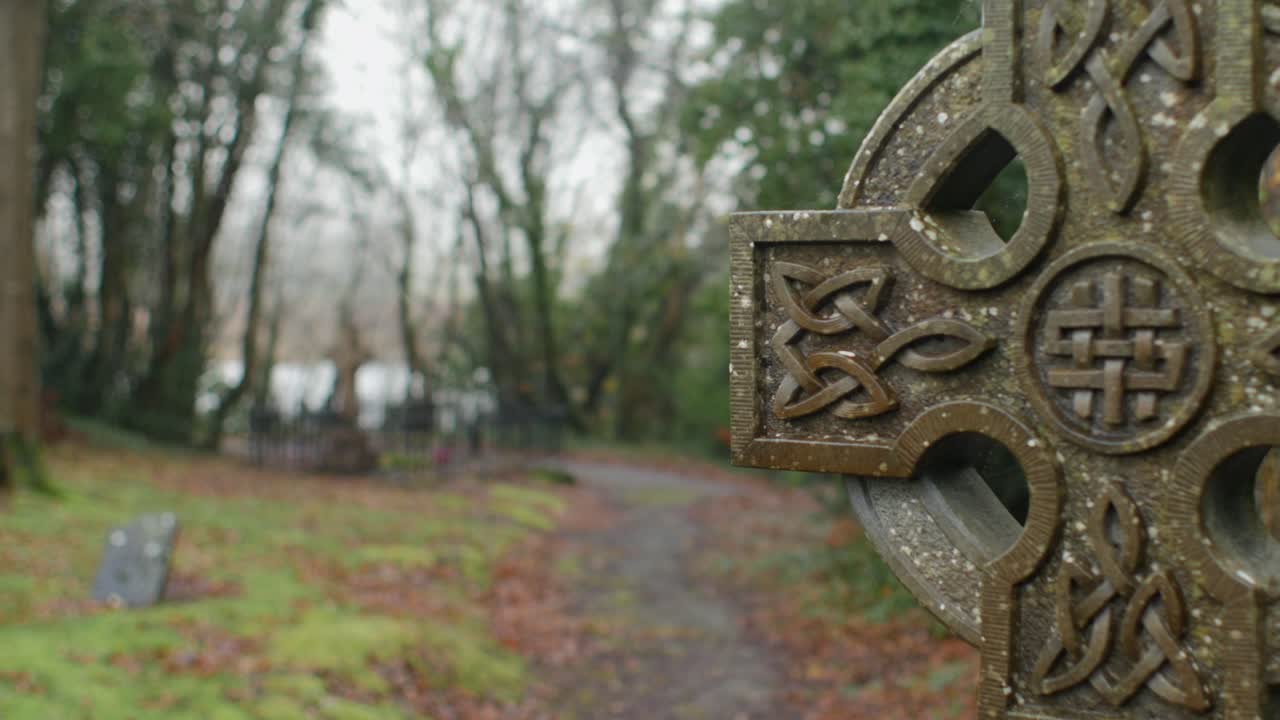 Static shot with pull focus on Celtic cross, isolated grave visible in background
