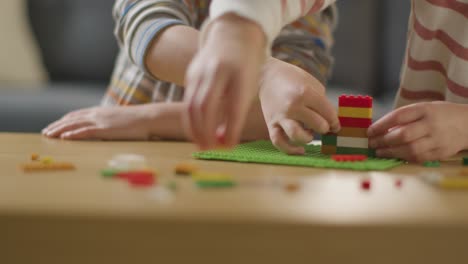 close up of two children playing with plastic construction bricks on table at home 3