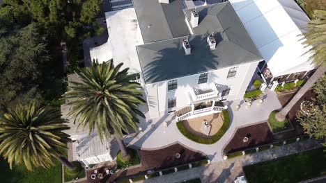 aerial circle view over a white villa with palms and flowerbeds around